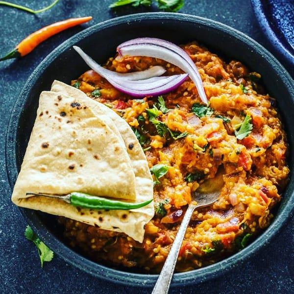 Baingan Bharta, an Indian eggplant dish, with flatbread, red onion, and chili in a black bowl.