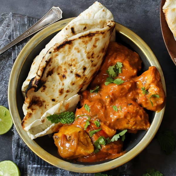 Spice Affair's butter chicken with naan bread, garnished with cilantro and mint, in a gold-rimmed bowl.