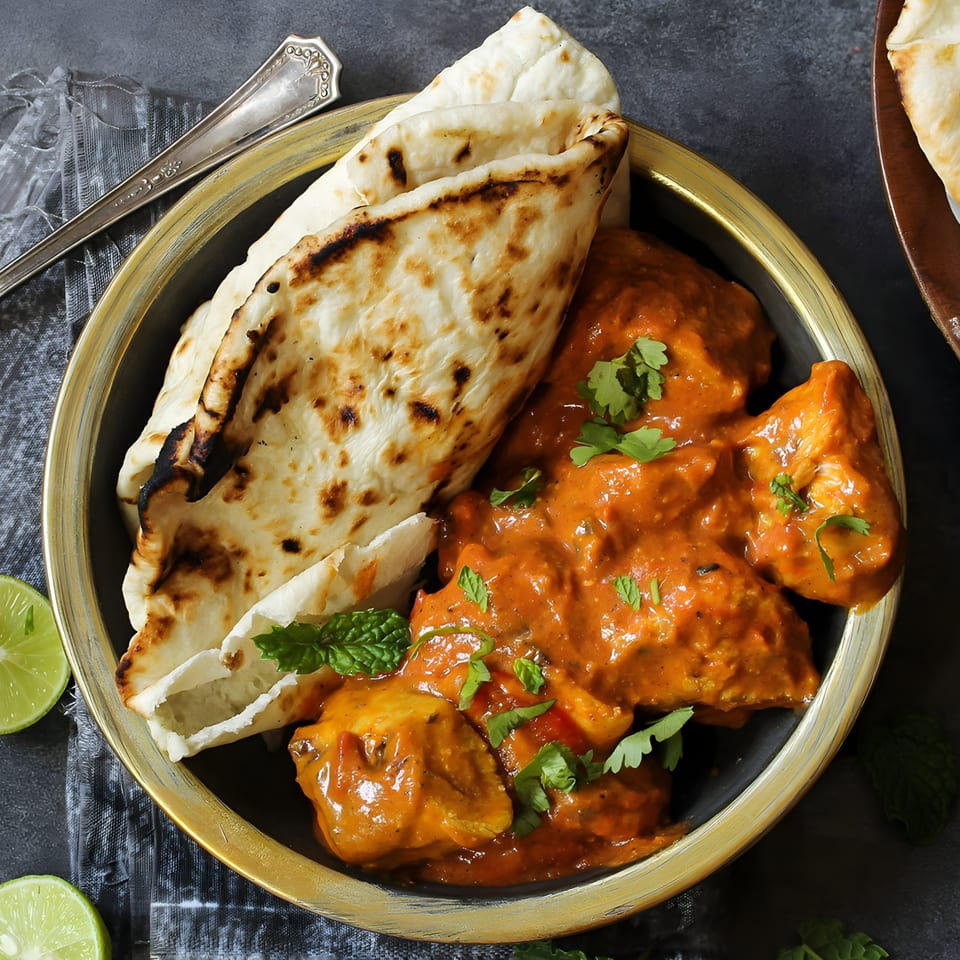 Spice Affair's butter chicken with naan bread, garnished with cilantro and mint, in a gold-rimmed bowl.