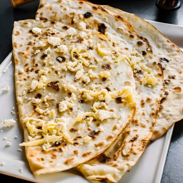 Close-up of three pieces of Indian naan bread topped with crumbled cheese on a white plate.