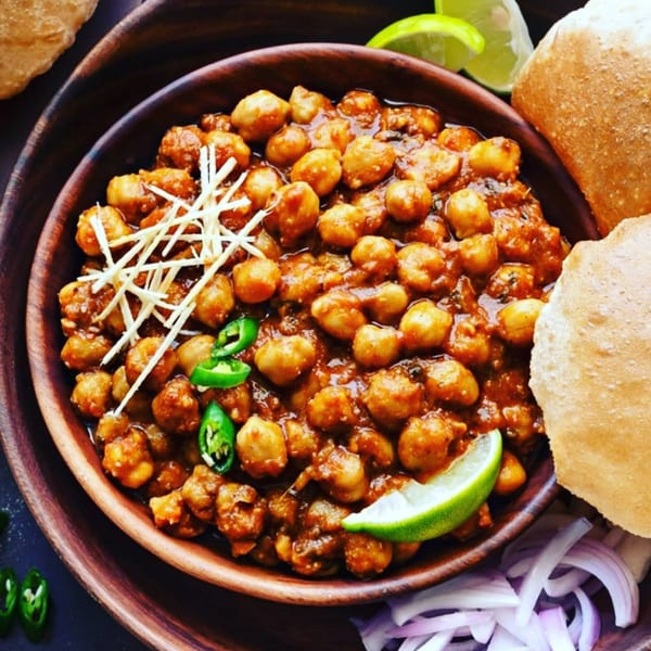A bowl of chana masala with ginger, green chilies, lime, and puri bread.